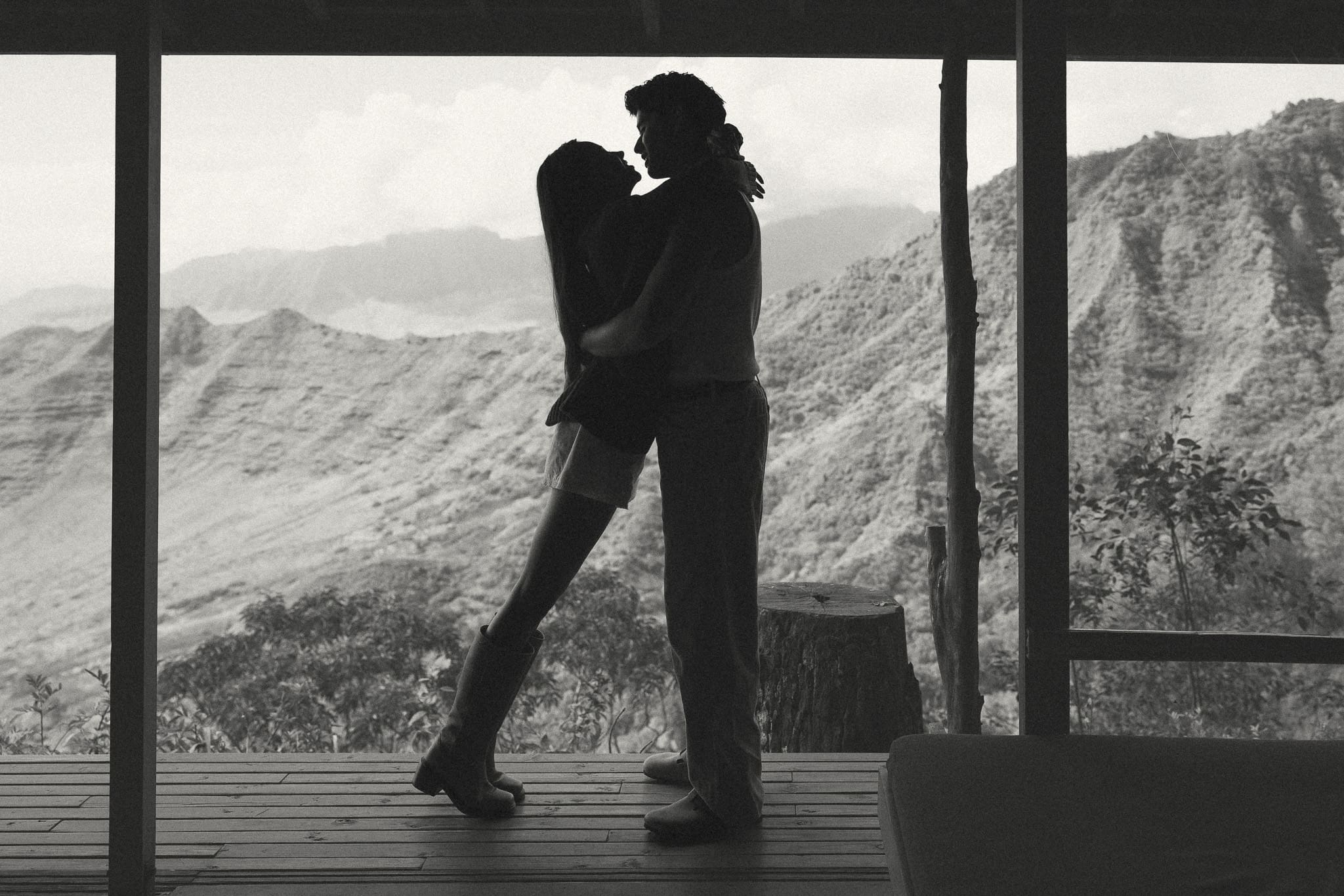a couple hugging and leaning in for a kiss overlooking the mountains. 
