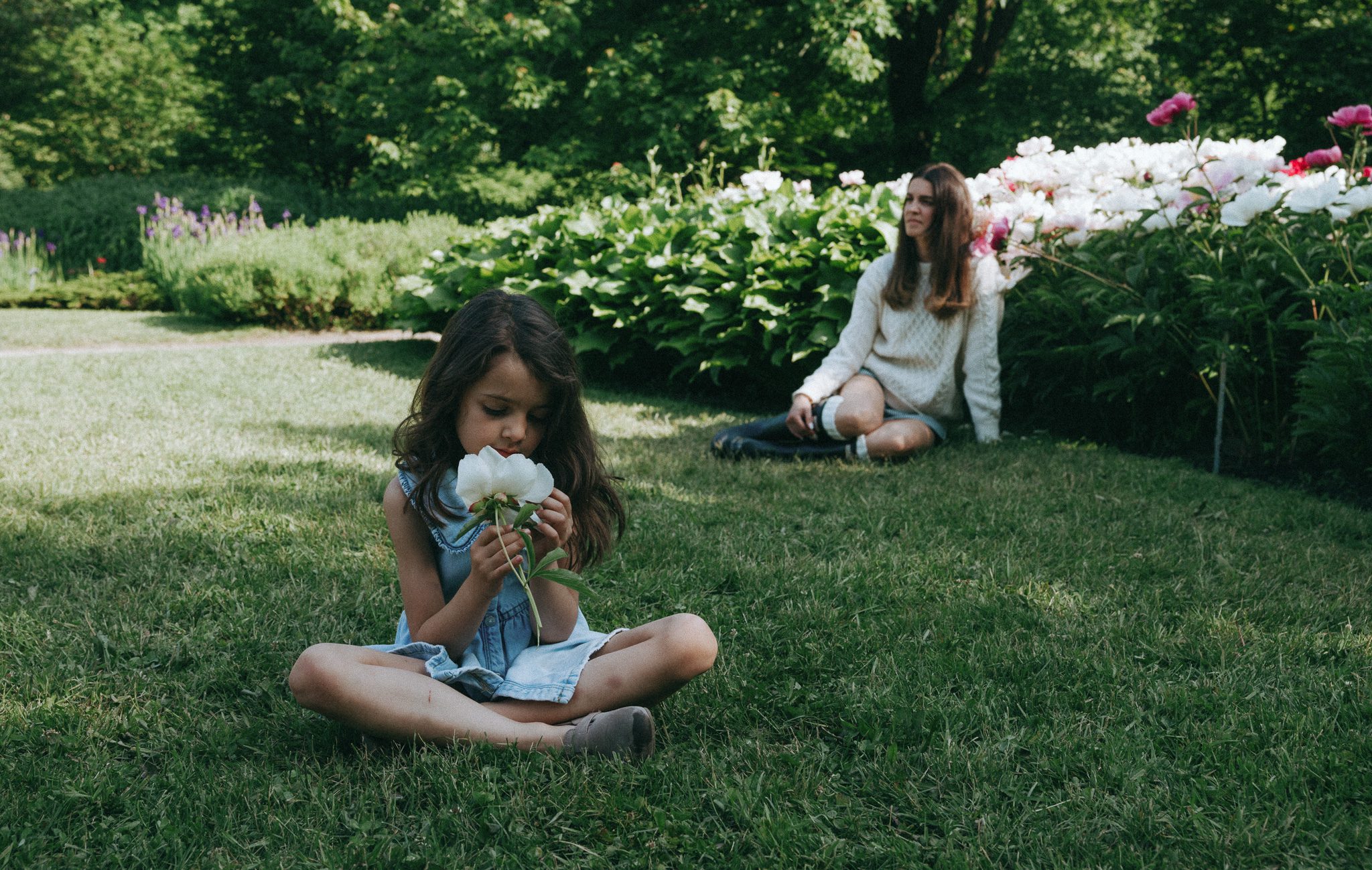 Mom sitting and girl smelling flowers on the grass for a family session in Montreal.