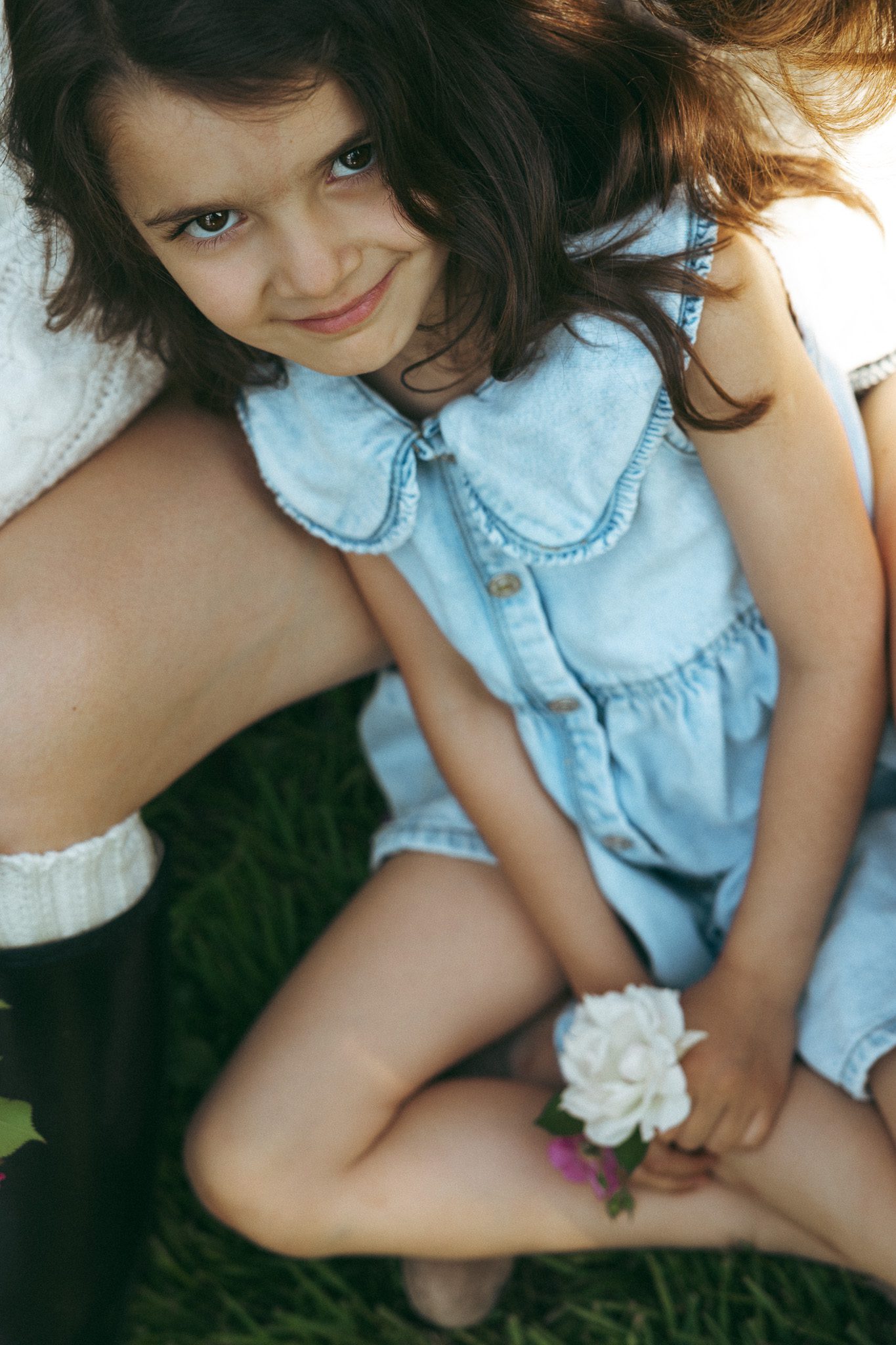 Girl holding flowers, in her mothers arms and smiling at the camera for a family photoshoot