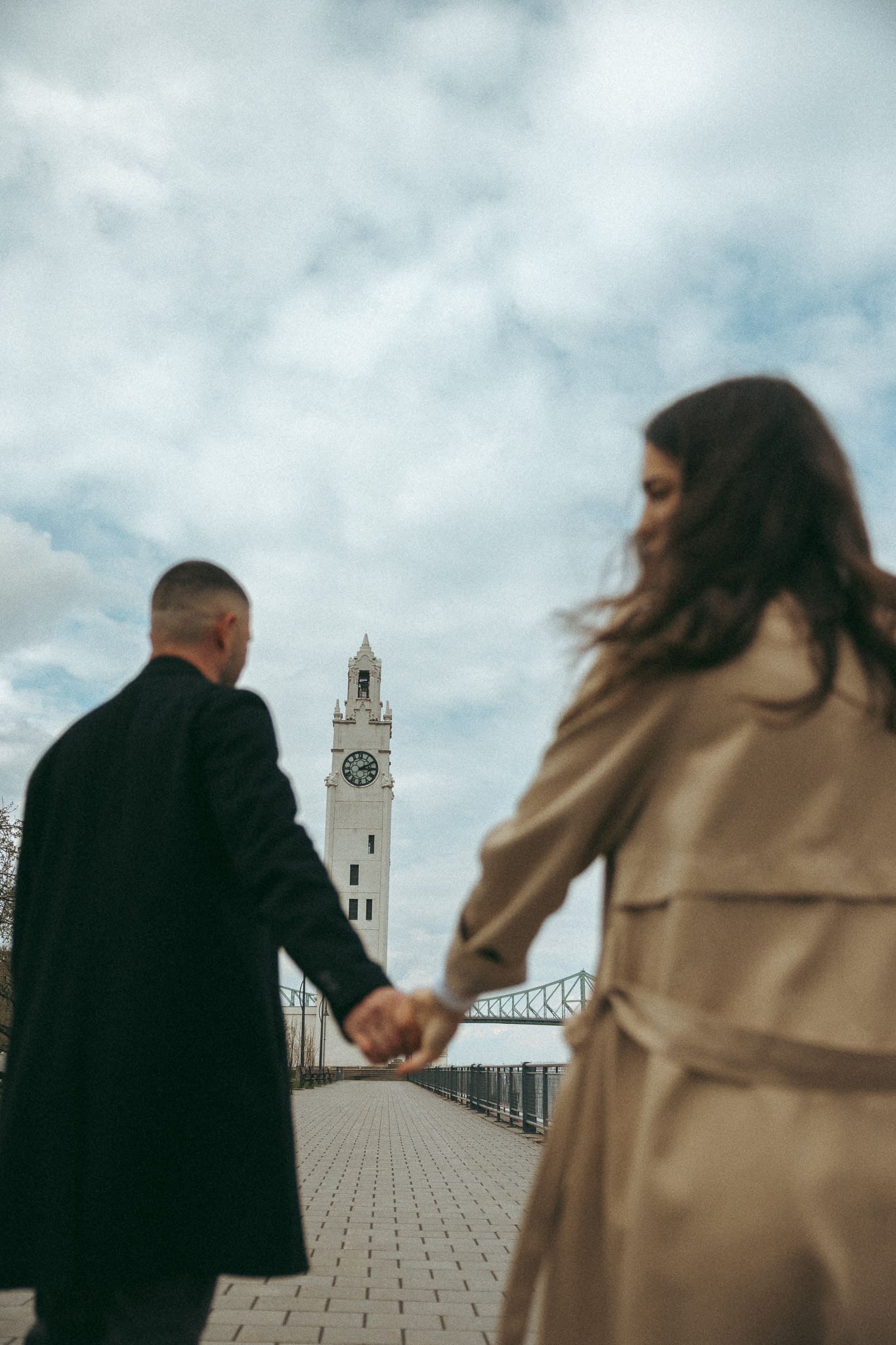 A couple holding hands and walking near the clock tower in old port Montreal for a couples session