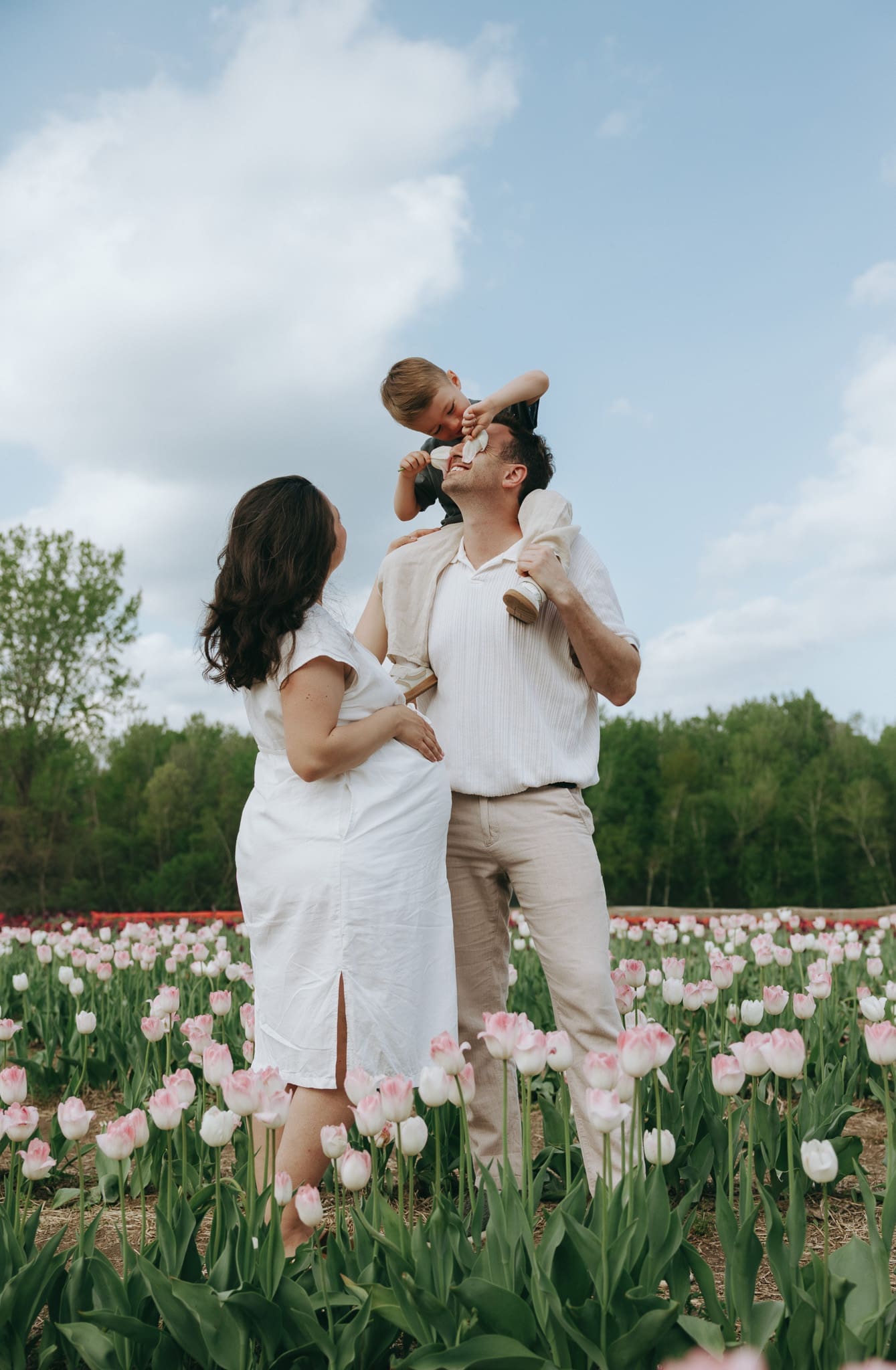Dad holds son up on his shoulders while son puts flowers on his face during a family session in Montreal